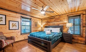 A bedroom with a wooden ceiling, a bed with a dark headboard, a nightstand, and a chair.