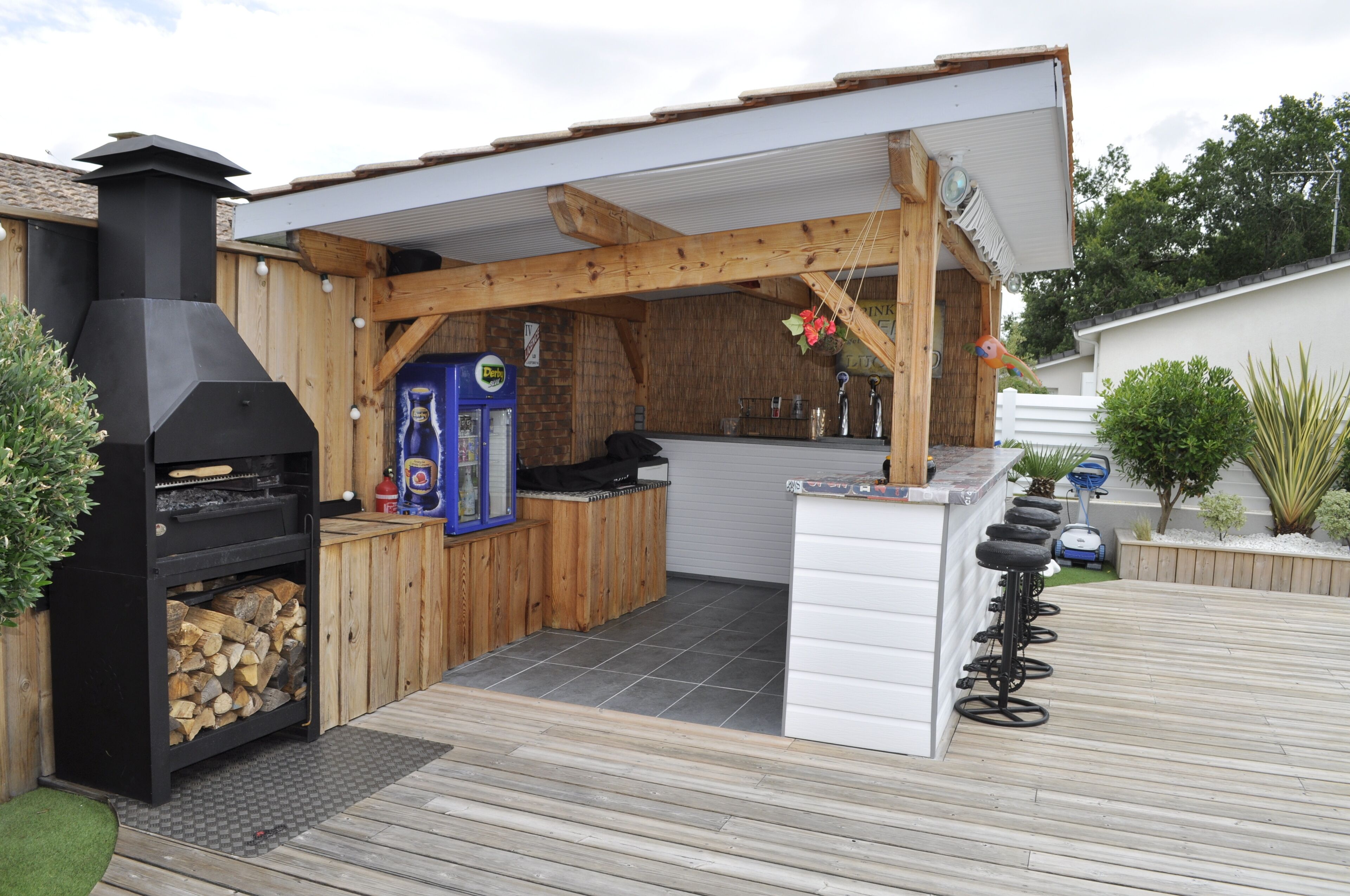 Een buitenkeuken met een barbecue, barkrukken en een houten terras.