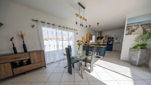 Une cuisine moderne dotée d’un îlot central, d’un coin repas avec une table en verre et d’une grande plante en pot.