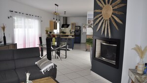 Un salon moderne avec un canapé, une table basse et une cheminée. On aperçoit, au fond, une cuisine avec un coin repas.