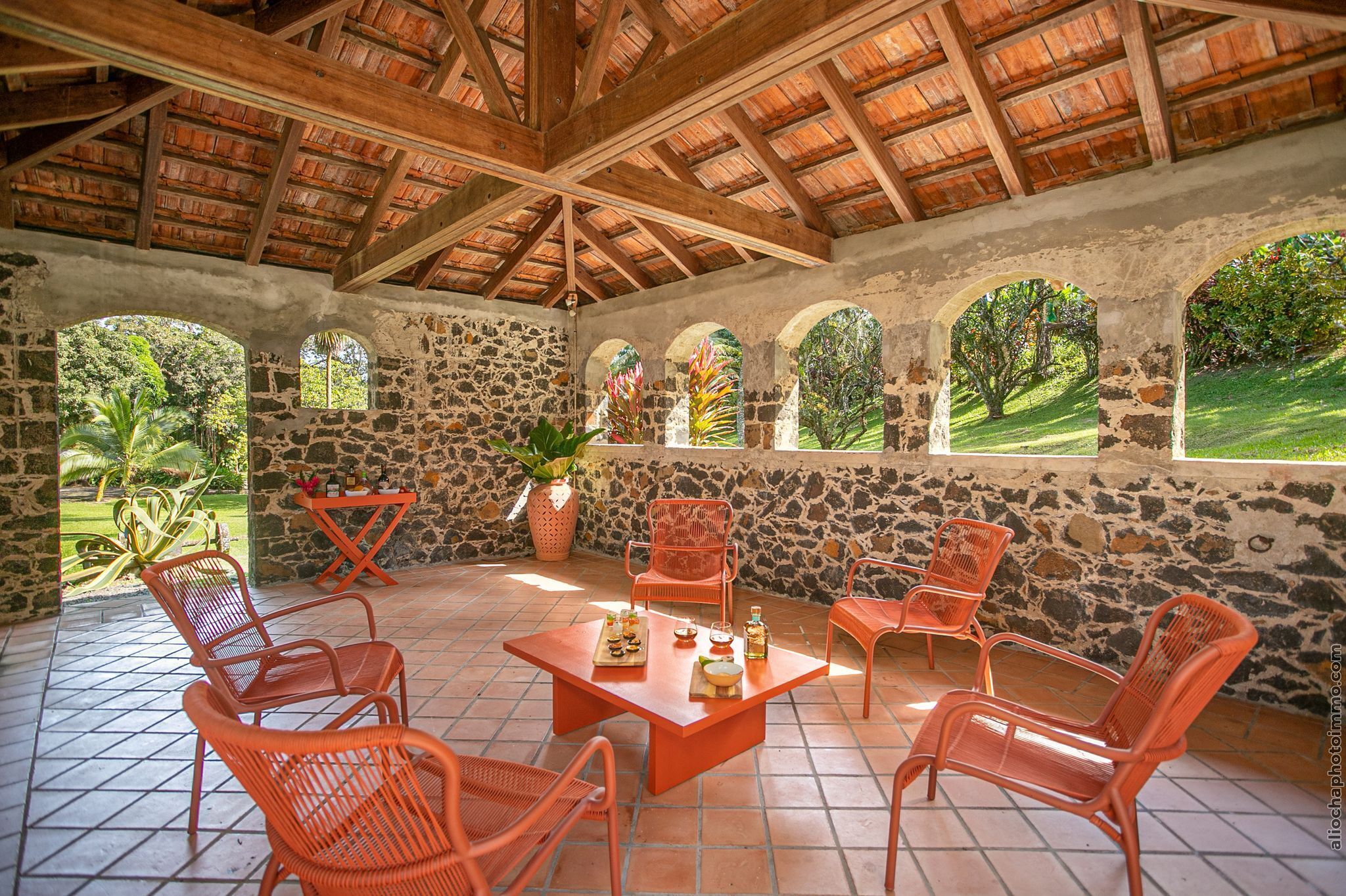 A covered patio with stone walls, wooden beams, and orange wicker furniture.