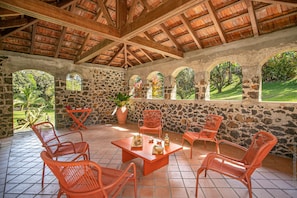 Un patio cubierto con paredes de piedra, vigas de madera y mobiliario de mimbre naranja.