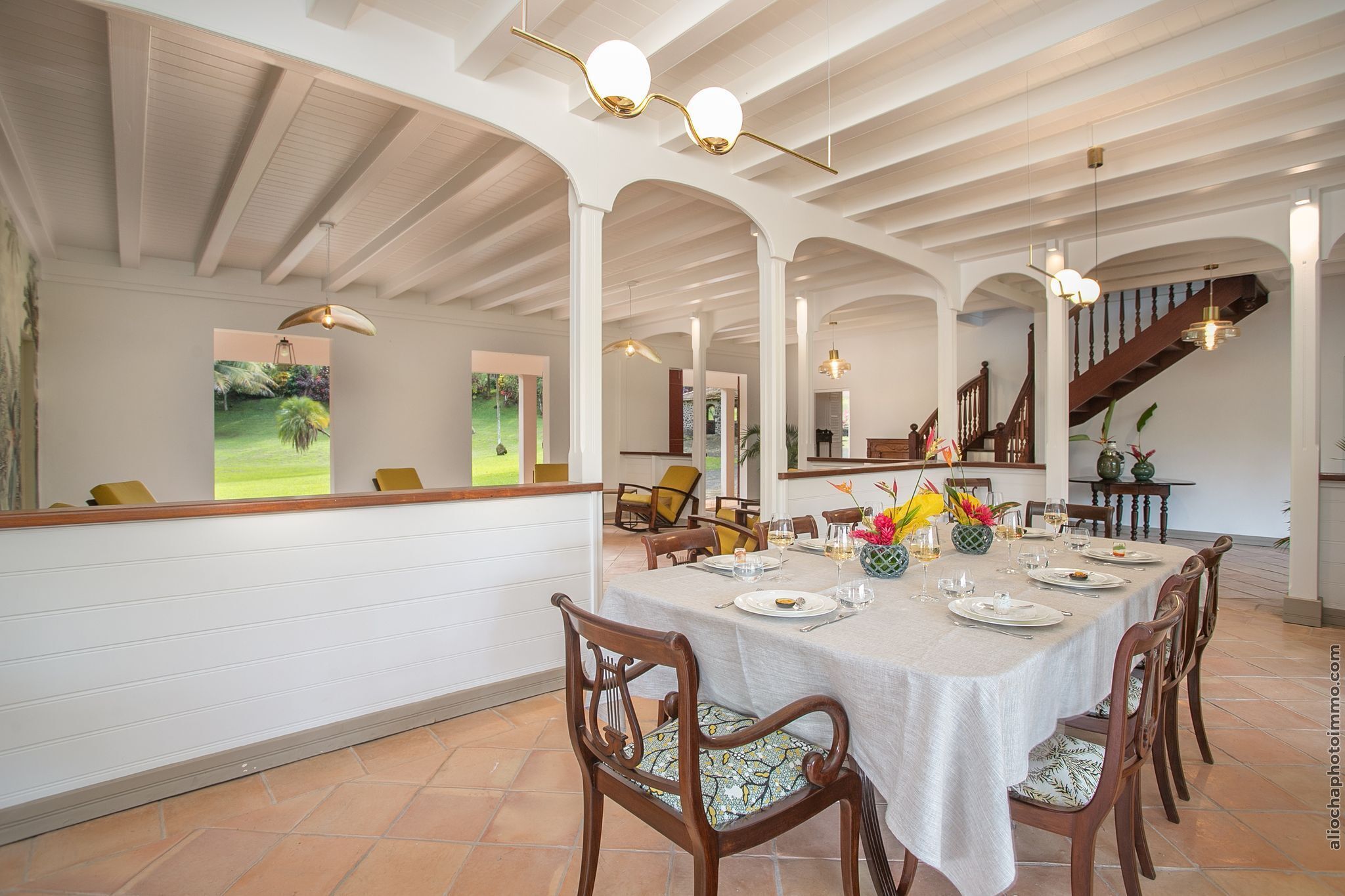 Uma sala de jantar com uma mesa comprida posta para uma refeição, rodeada por cadeiras de madeira.