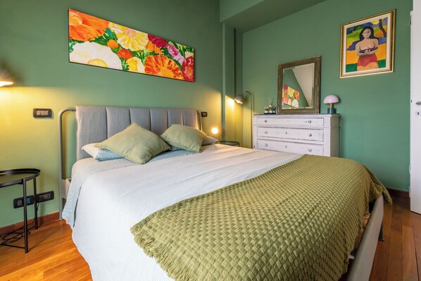 Un dormitorio con cama, mesita de noche, cómoda y obras de arte en las paredes.