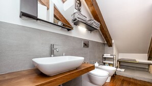 Moderni kylpyhuone, jossa on suuri valkoinen pesuallas, wc ja puinen allaskaappi.