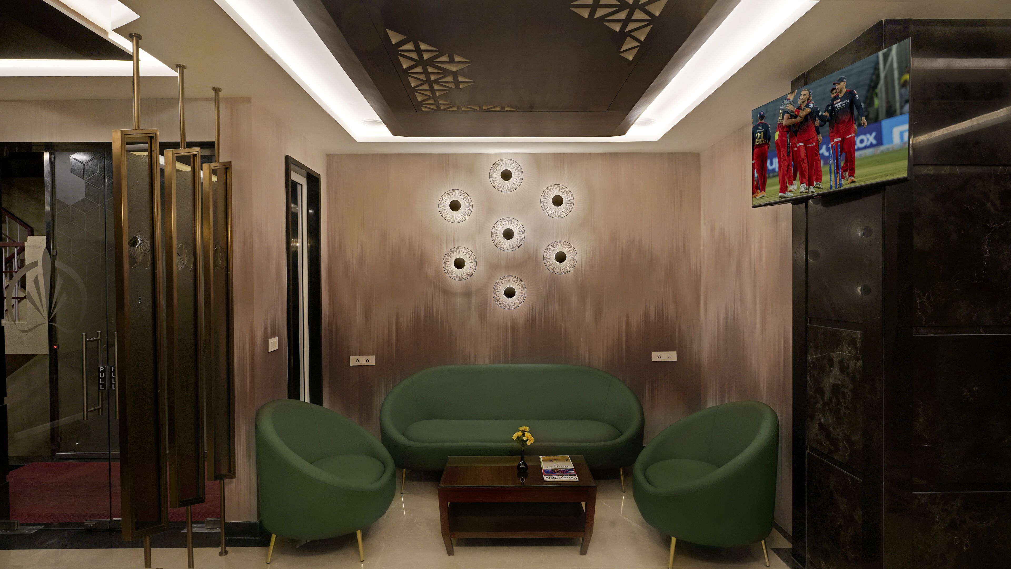Un vestíbulo moderno con un sofá verde, dos sillones, una mesita de centro y un techo con diseños geométricos.