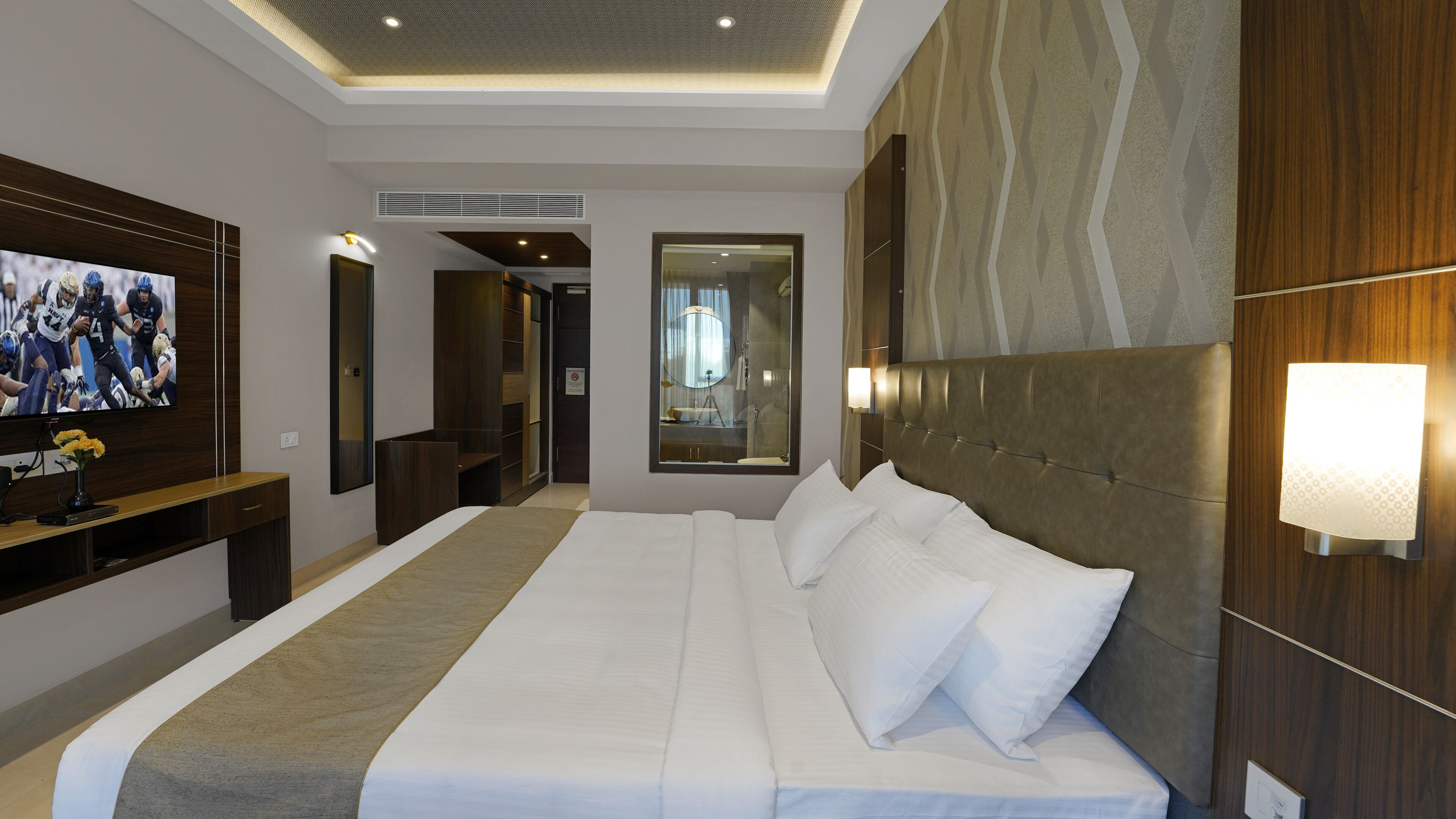 Une chambre d’hôtel moderne dotée d’un grand lit, d’une télévision à écran plat, d’une coiffeuse avec miroir et d’un dressing.