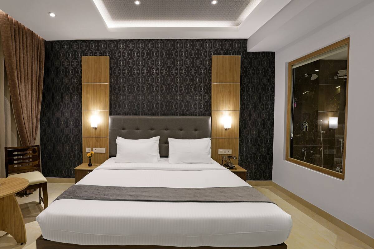 Une chambre d’hôtel moderne avec un grand lit, deux tables de chevet, une petite table, un bureau et une grande fenêtre.