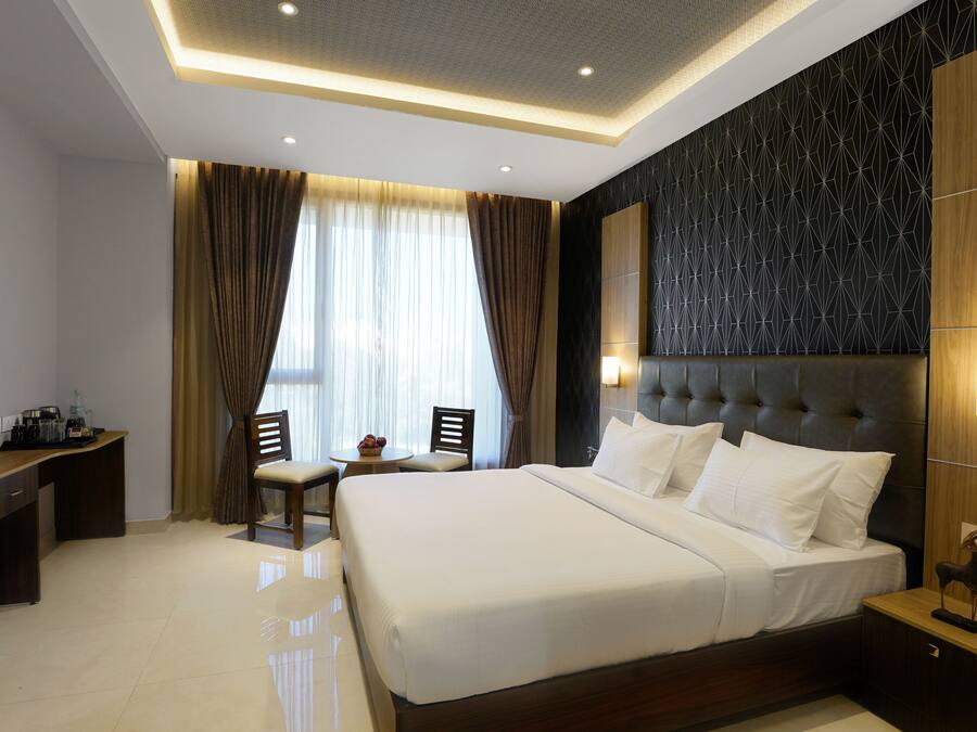Habitación de hotel moderna con una cama grande, un televisor mostrando noticias deportivas, un escritorio con computadora y un área de descanso con sillas.