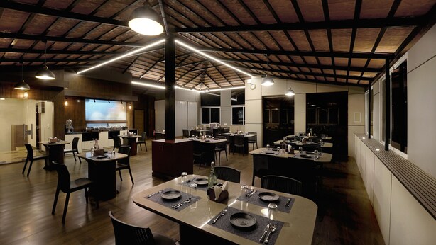 Un restaurante espacioso con techos altos e iluminación moderna. Las mesas están dispuestas con platos, cubiertos y vasos.