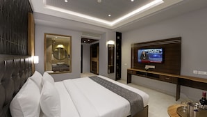 Una habitación de hotel moderna con una cama grande, un televisor que muestra noticias deportivas, un tocador con espejo y una mesa consola de madera.