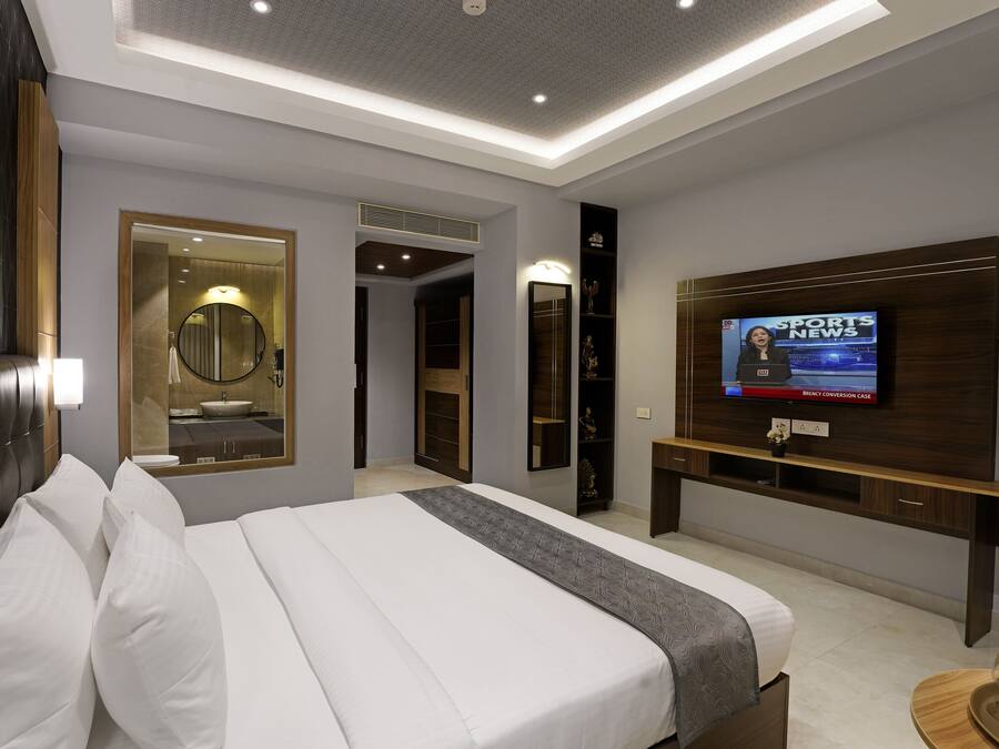 Una habitación de hotel moderna con una cama grande, un televisor que muestra noticias deportivas, un tocador con espejo y una mesa consola de madera.