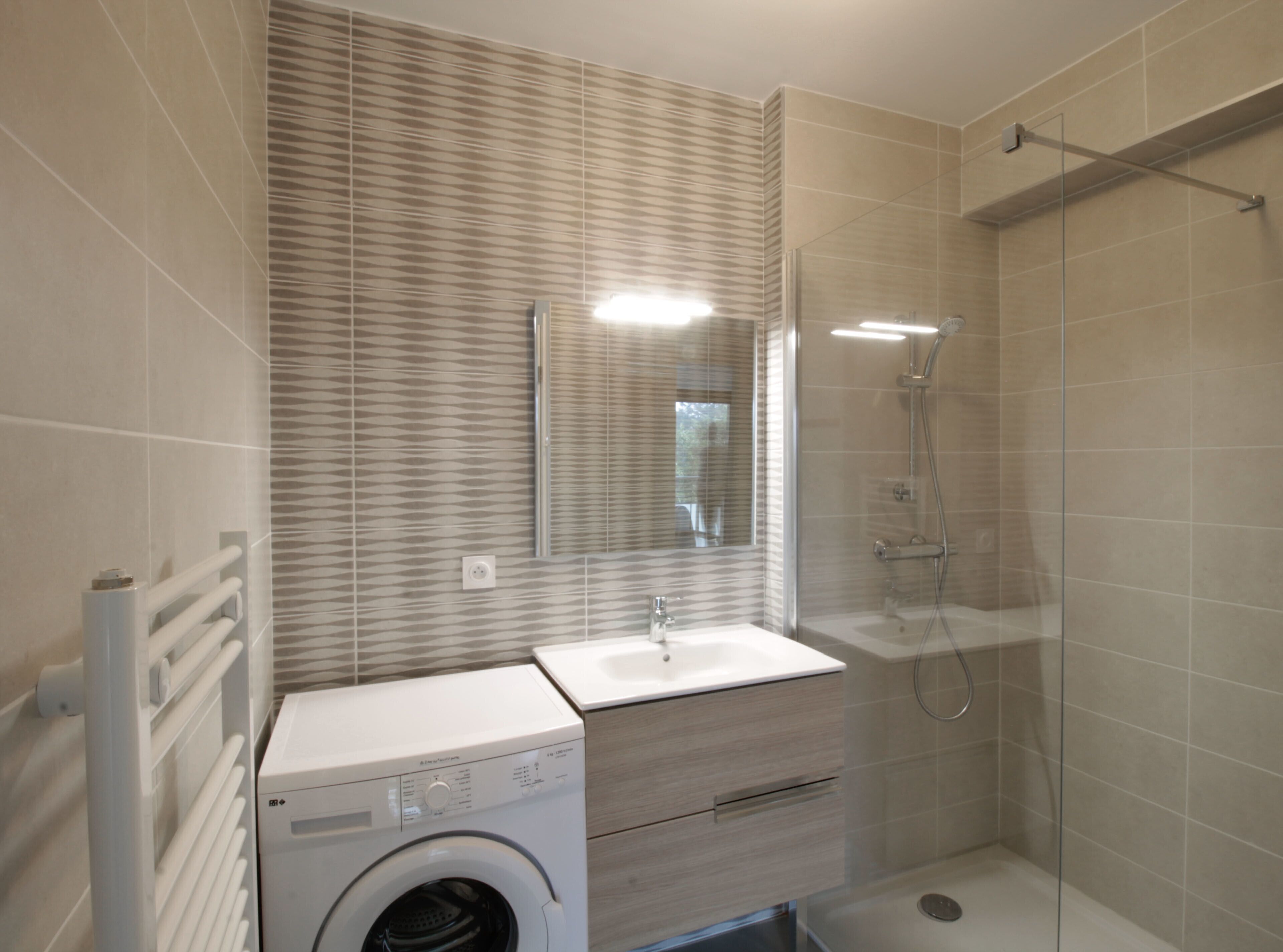 A modern bathroom with a built-in washing machine, a glass shower enclosure, and a vanity with a mirror.