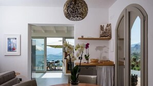 A modern dining area with a round wooden table, chairs, and a vase of orchids. - Villa Magliolo (Cefalù)