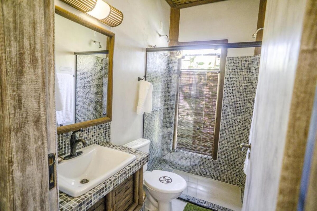 Un baño con cabina de ducha revestida de mosaicos, un lavabo blanco y un inodoro.