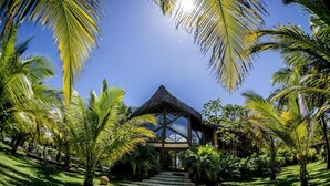 A tropical resort with a thatched-roof structure, surrounded by palm trees and a well-maintained lawn.