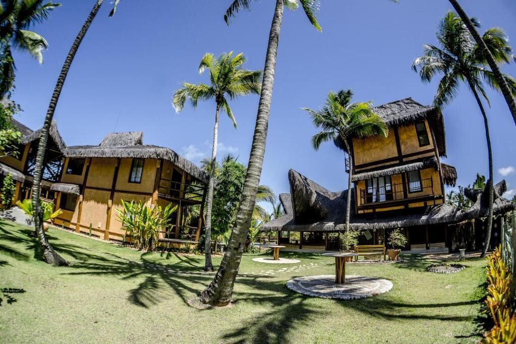 Un resort con edifici a tetto di paglia, palme e una zona salotto circolare.