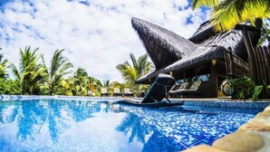 A swimming pool with a thatched roof structure and lounge chairs.