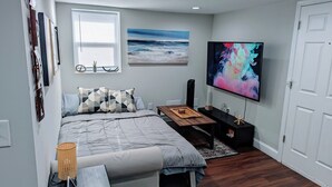 Une chambre à coucher moderne avec un lit, une table de chevet, une télévision et une œuvre d’art accrochée au mur.