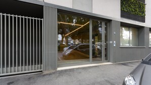 Una entrada moderna de edificio con puerta de vidrio, una cerca metálica y un coche estacionado en frente.