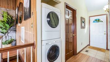 A laundry room with stacked washers and dryers, wooden walls, and a door with a decorative glass panel.