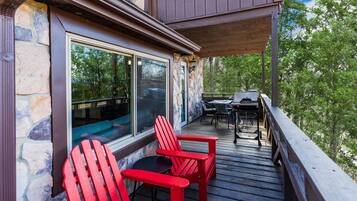 A wooden deck with red Adirondack chairs and a table, overlooking a forested area.