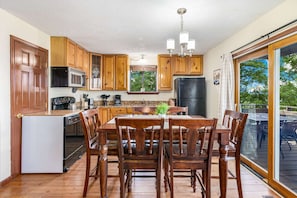 Une cuisine avec des meubles en bois, une table à manger avec des chaises, un réfrigérateur, un four à micro-ondes et une fenêtre donnant sur des arbres.