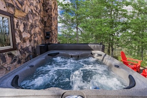 Un bain à remous avec un mur extérieur en pierre, entouré d’arbres et agrémenté d’une chaise rouge.