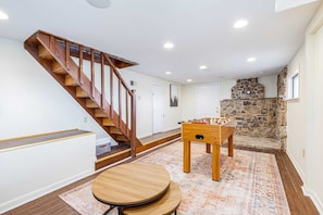 A spacious room with a wooden staircase, a foosball table, and a stone fireplace. - Stone chalet w/ views & hot tub (Gerrardstown)