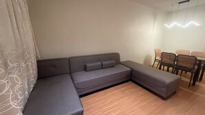 A modern living room with a grey sectional sofa, a dining table with chairs, and a light fixture on the ceiling. - Comfy Family Condo in Resort Condo! (Davao City)