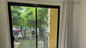 A bedroom with a bed, a window with a view of a balcony, and a curtain. - Comfy Family Condo in Resort Condo! (Davao City)