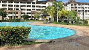 A hotel with a swimming pool, palm trees, and a clear blue sky. - Comfy Family Condo in Resort Condo! (Davao City)