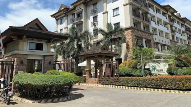 A multi-story residential building with balconies, a gated entrance, and a well-maintained garden area. - Comfy Family Condo in Resort Condo! (Davao City)