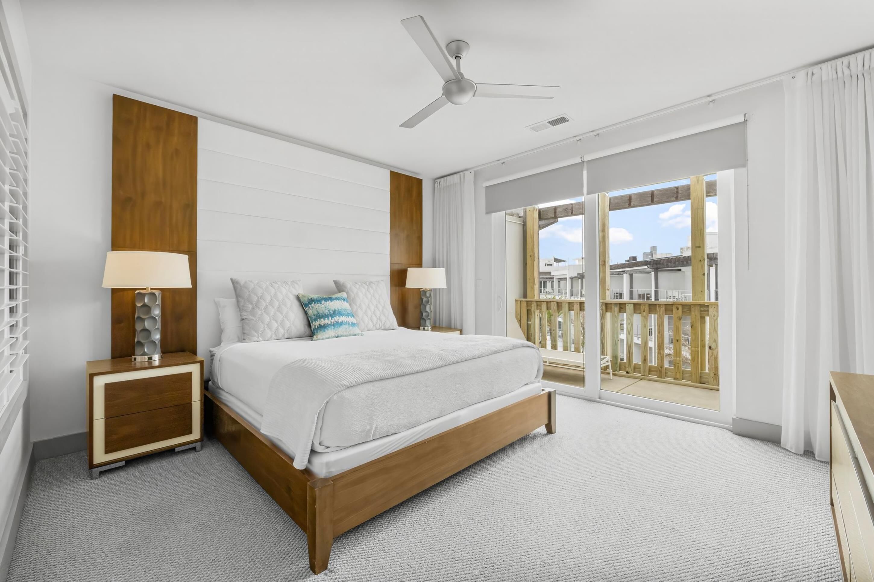 A modern hotel room with a large bed, two bedside tables with lamps, a ceiling fan, and a balcony with a view of the city.