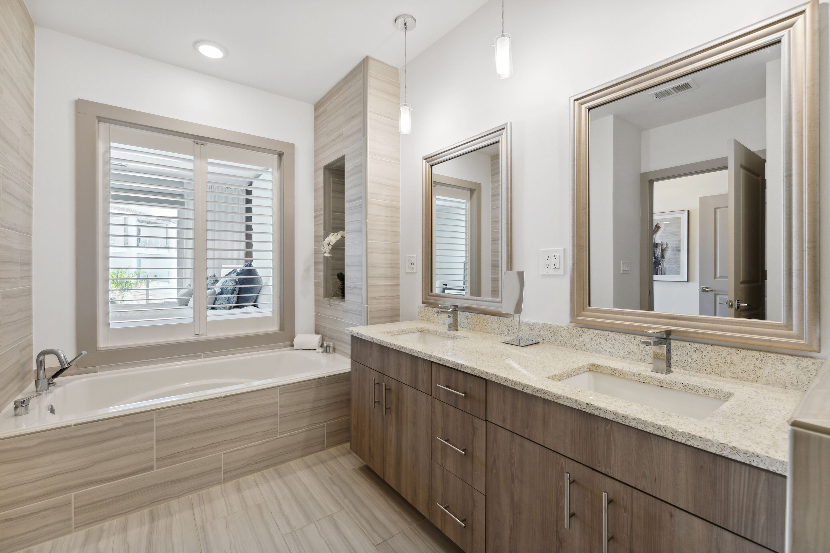 Un baño moderno con una bañera grande, tocador doble con espejo y ventana con persianas.