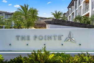 Ein Schild mit der Aufschrift "THE POINTE" und einem Stern, umgeben von Palmen und einem Gebäude mit Balkonen.