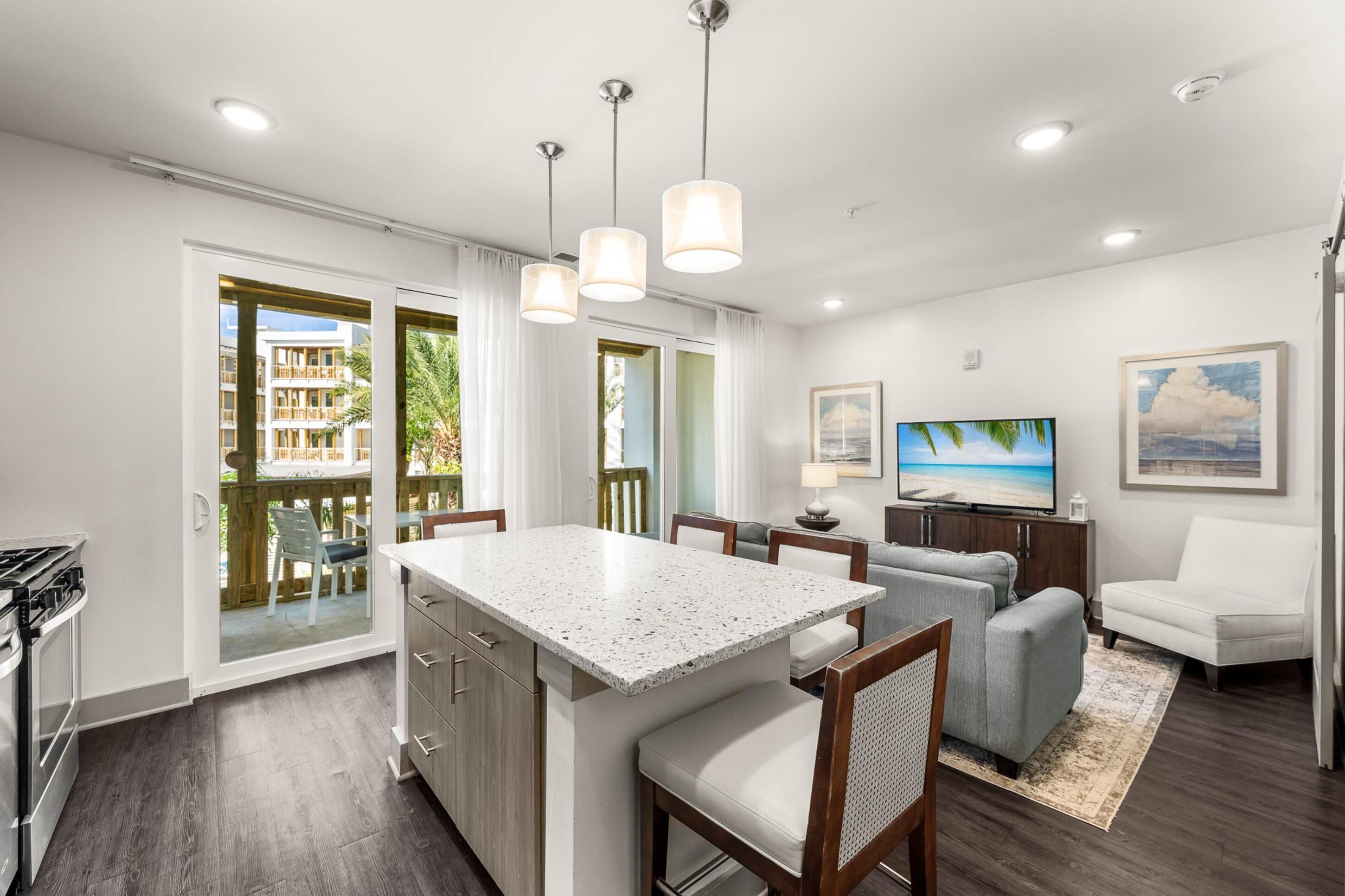 Una cocina moderna con una isla central, zona de comedor con sillas, un televisor y un sofá.