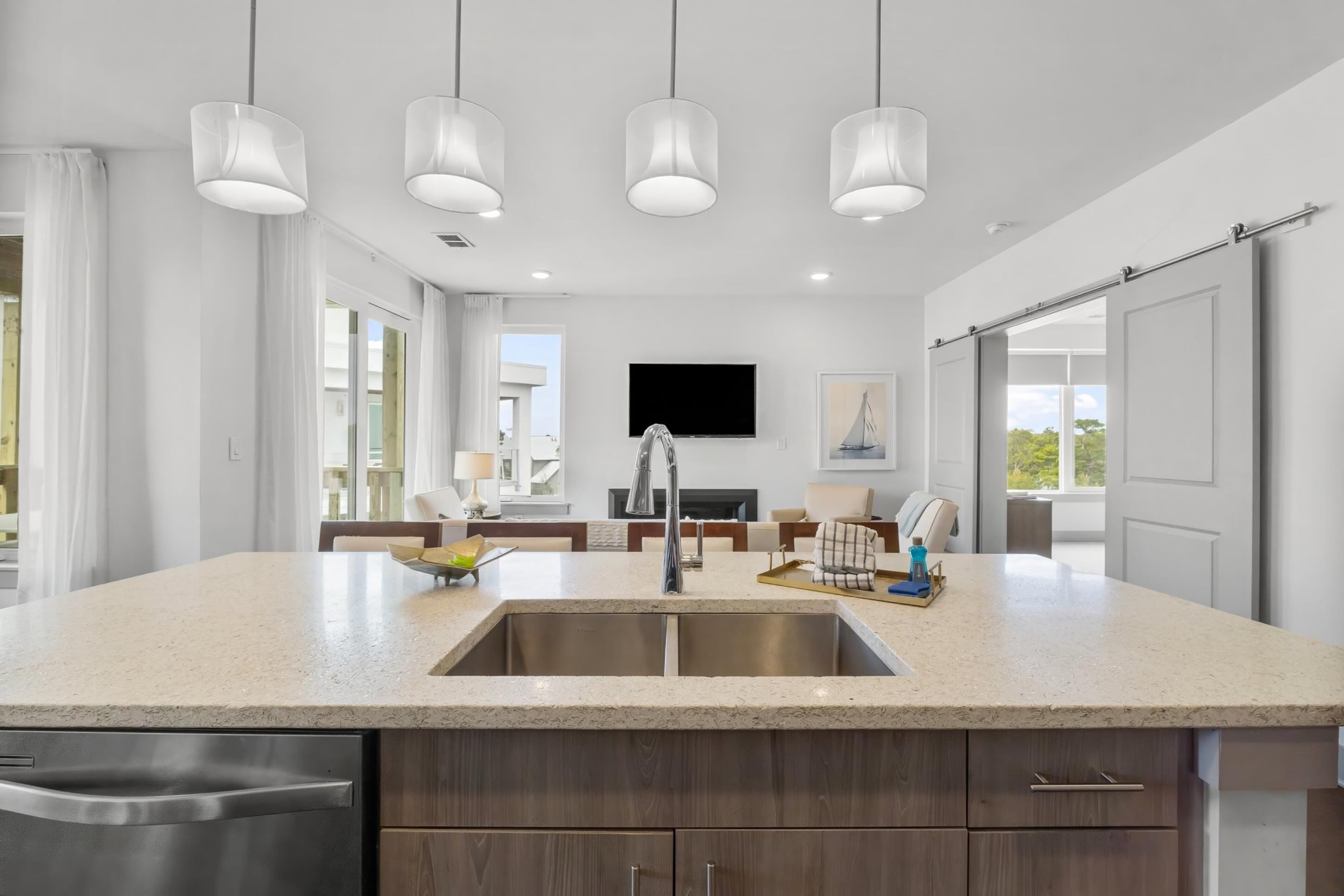 A modern kitchen with a large island, stainless steel appliances, pendant lighting, and a view to the living area.