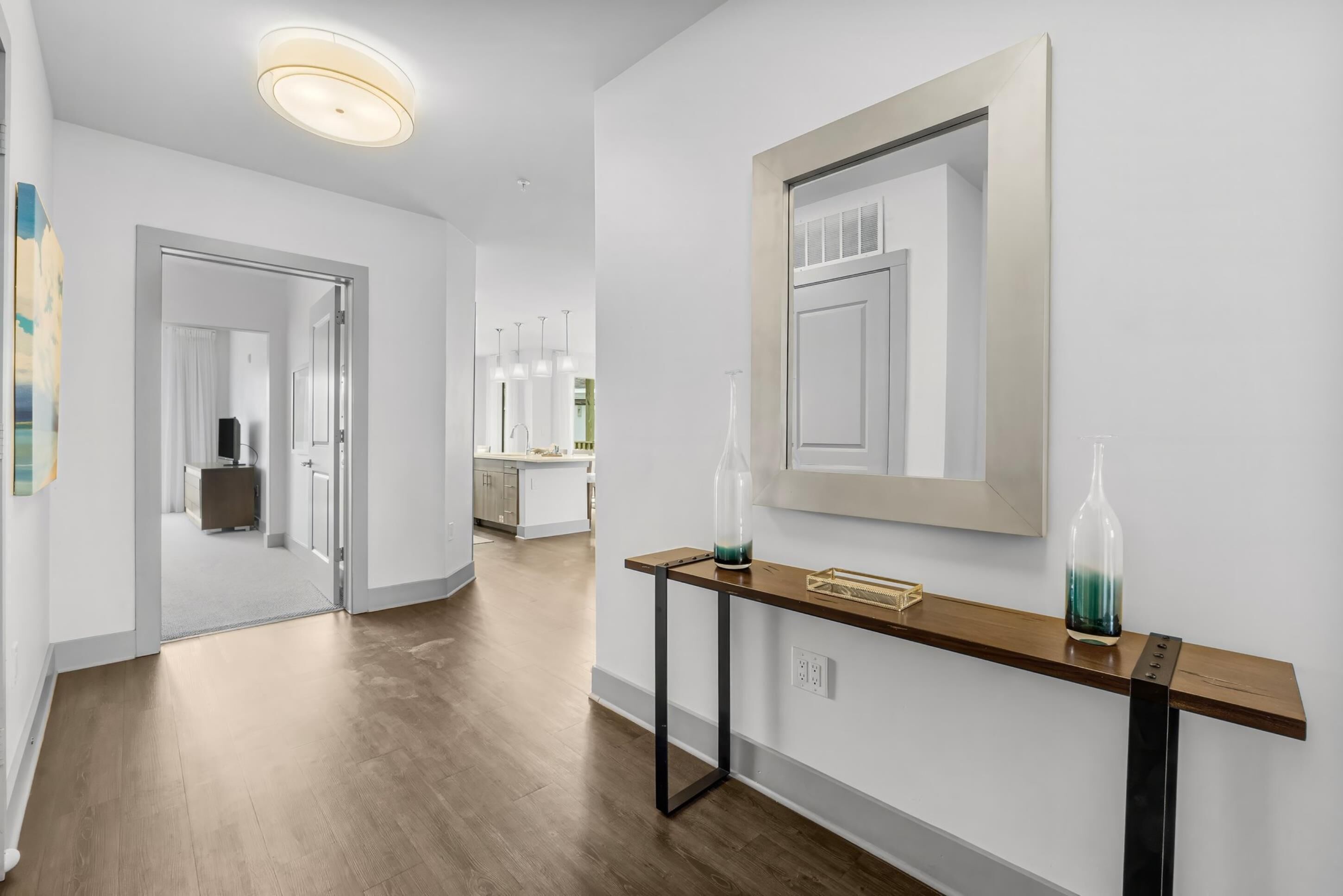 A modern hallway with a wooden floor, a console table with decorative bottles, and a large mirror on the wall.