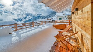 Um deck de madeira com guarda-corpo de madeira, uma parede de madeira e vista para montanhas cobertas de neve.