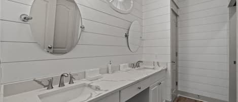 Moderni kylpyhuone, jossa on kaksi pesuallasta, suuri peili ja ovi, joka johtaa toiseen huoneeseen.