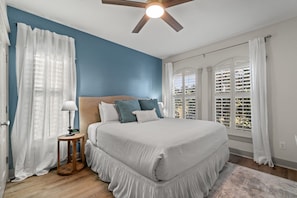 A bedroom with a large bed, a ceiling fan, and a view of a parking garage through the window.