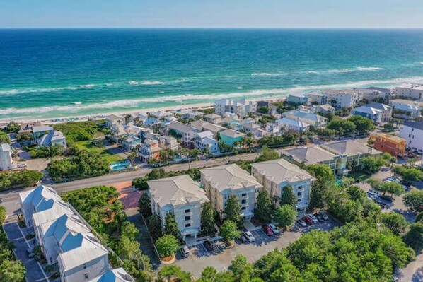 An aerial view of a coastal town with residential buildings, a beach, and a clear view of the ocean.