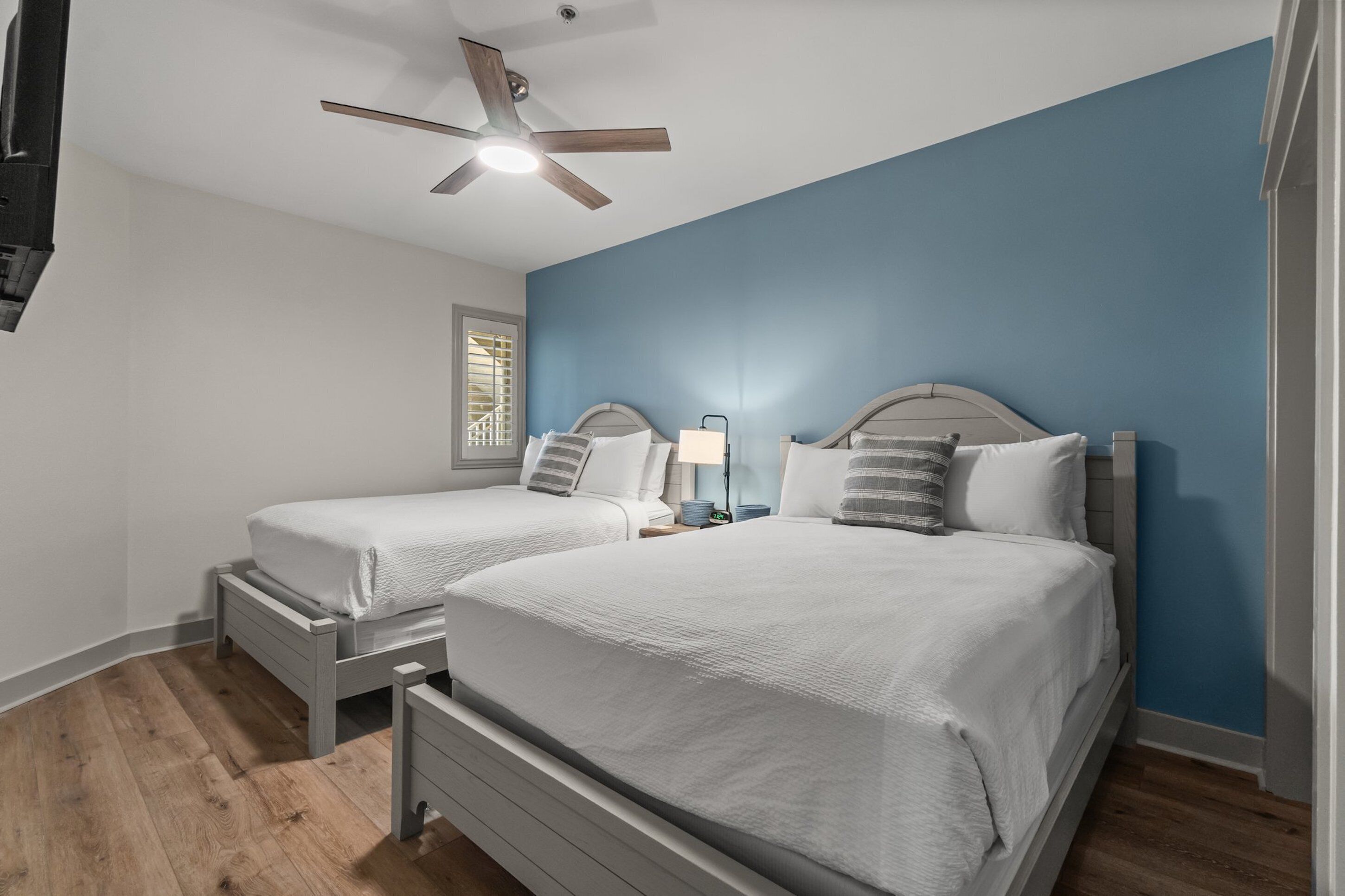 A bedroom with two beds, a ceiling fan, and a window with blinds.