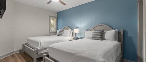 A bedroom with two beds, a ceiling fan, and a window with blinds.