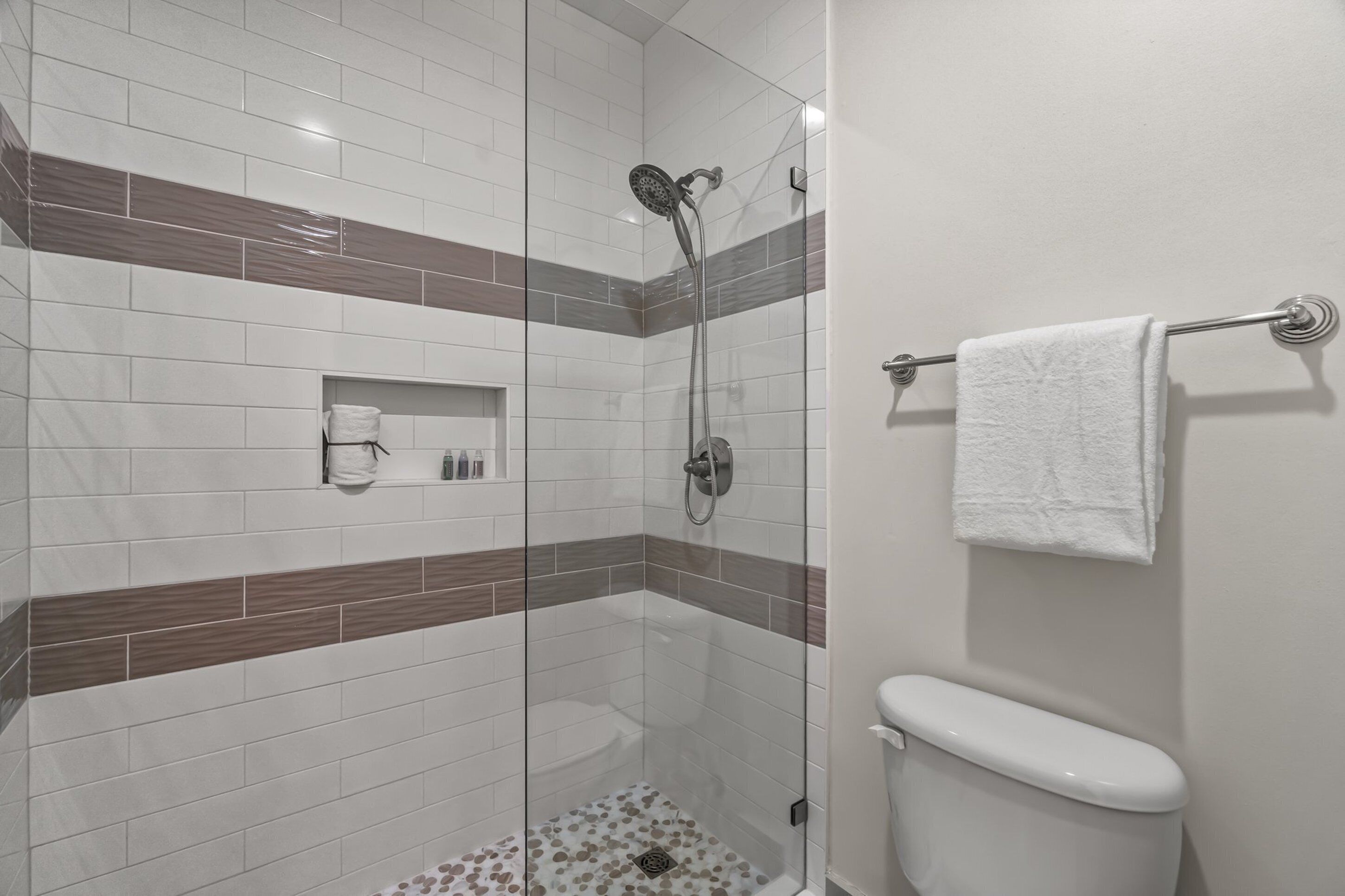 A modern bathroom with a glass-enclosed shower, white tiles, and a toilet.