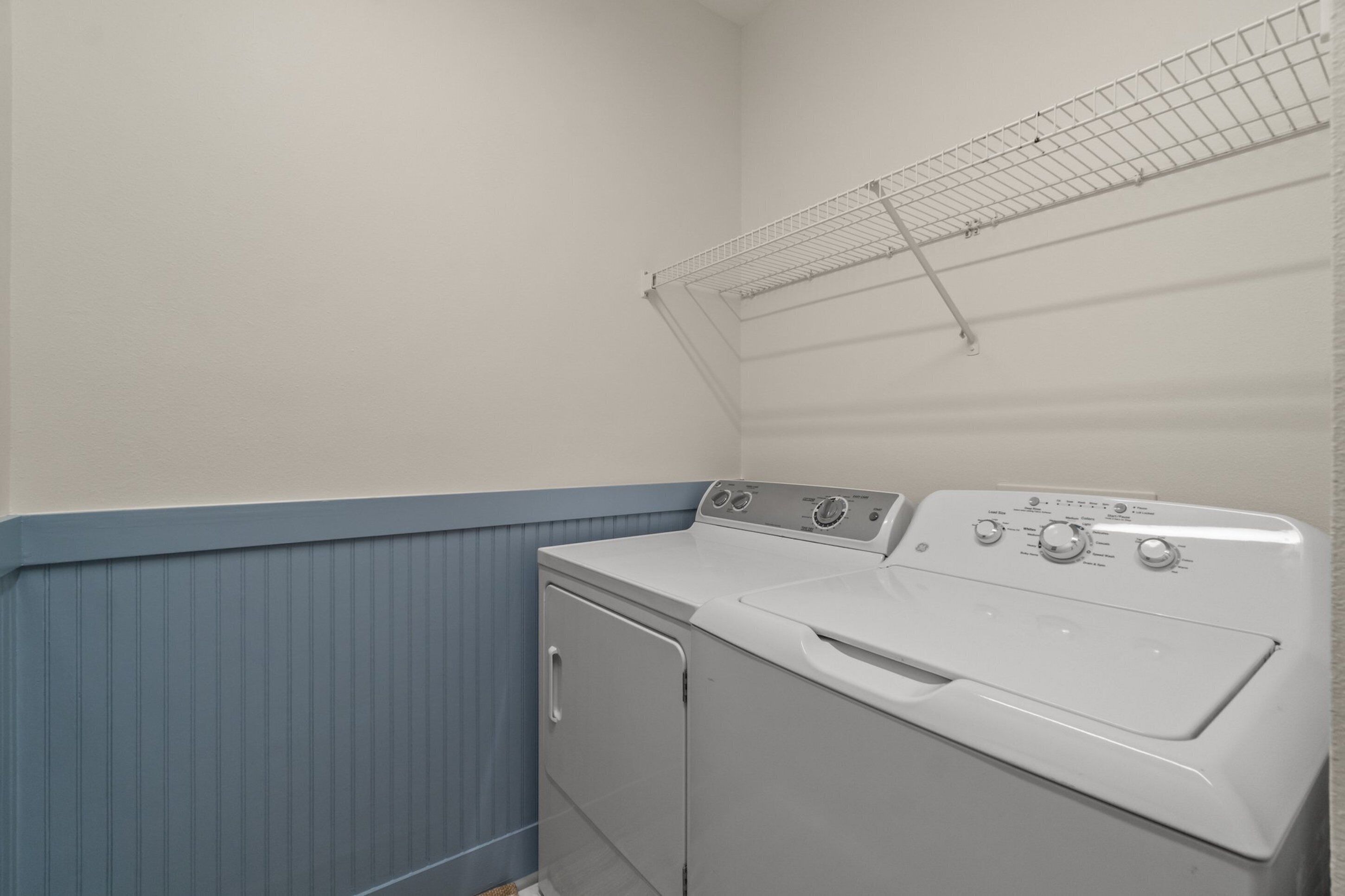 A laundry room with a front-loading washer and dryer, a drying rack, and a blue baseboard.