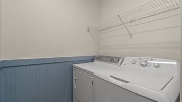 A laundry room with a front-loading washer and dryer, a drying rack, and a blue baseboard.