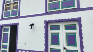 A two-story building with a white facade and purple accents, featuring multiple windows with green and gold trim, and a door with similar decorative elements. - House F - Beautiful House Traditional Facade - Modern Interior (Filandia)
