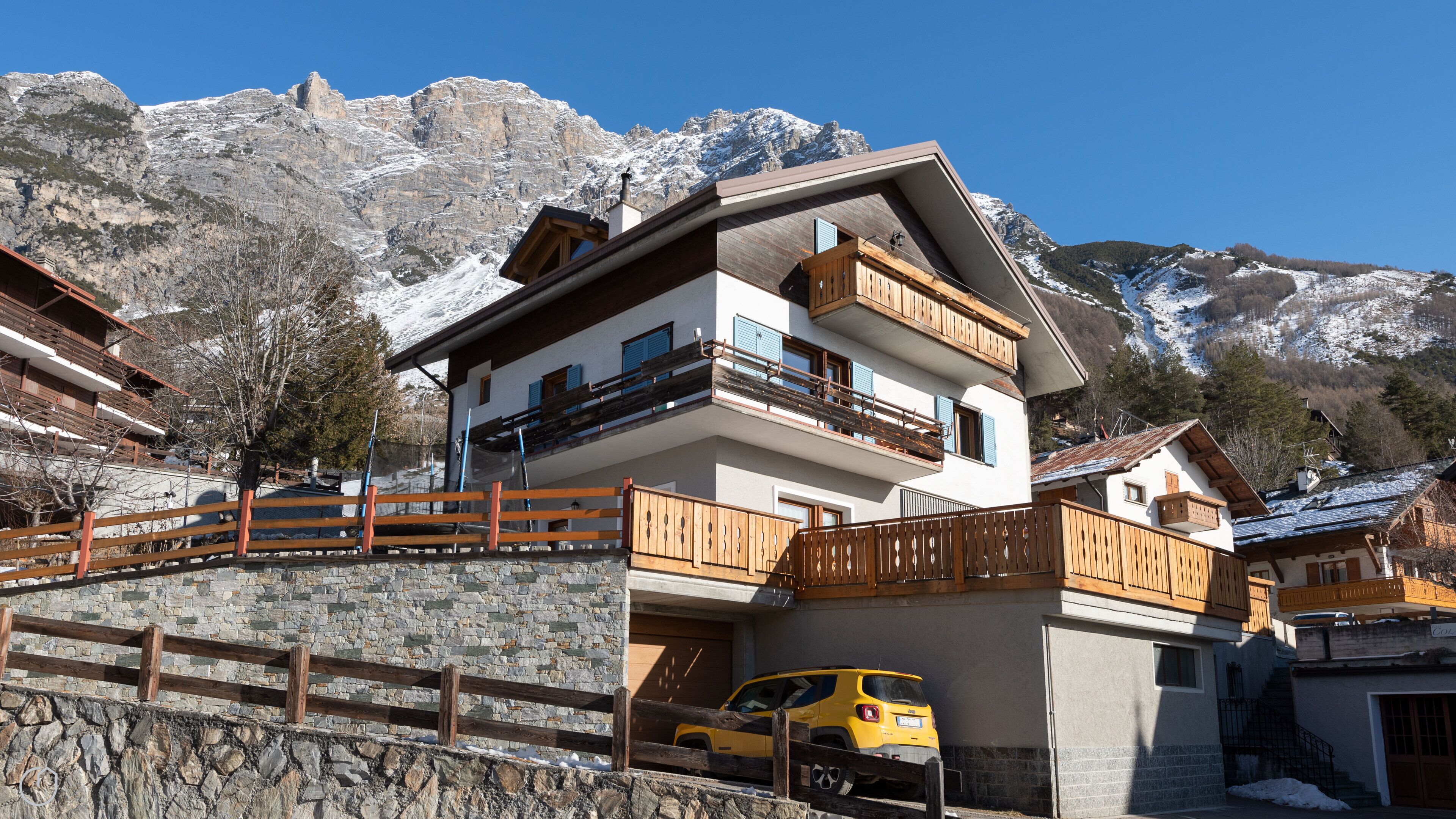 A multi-story building with balconies, a stone wall, and a parked yellow car.